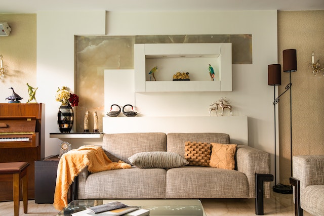 beige couch and piano in a living room with orange decor details